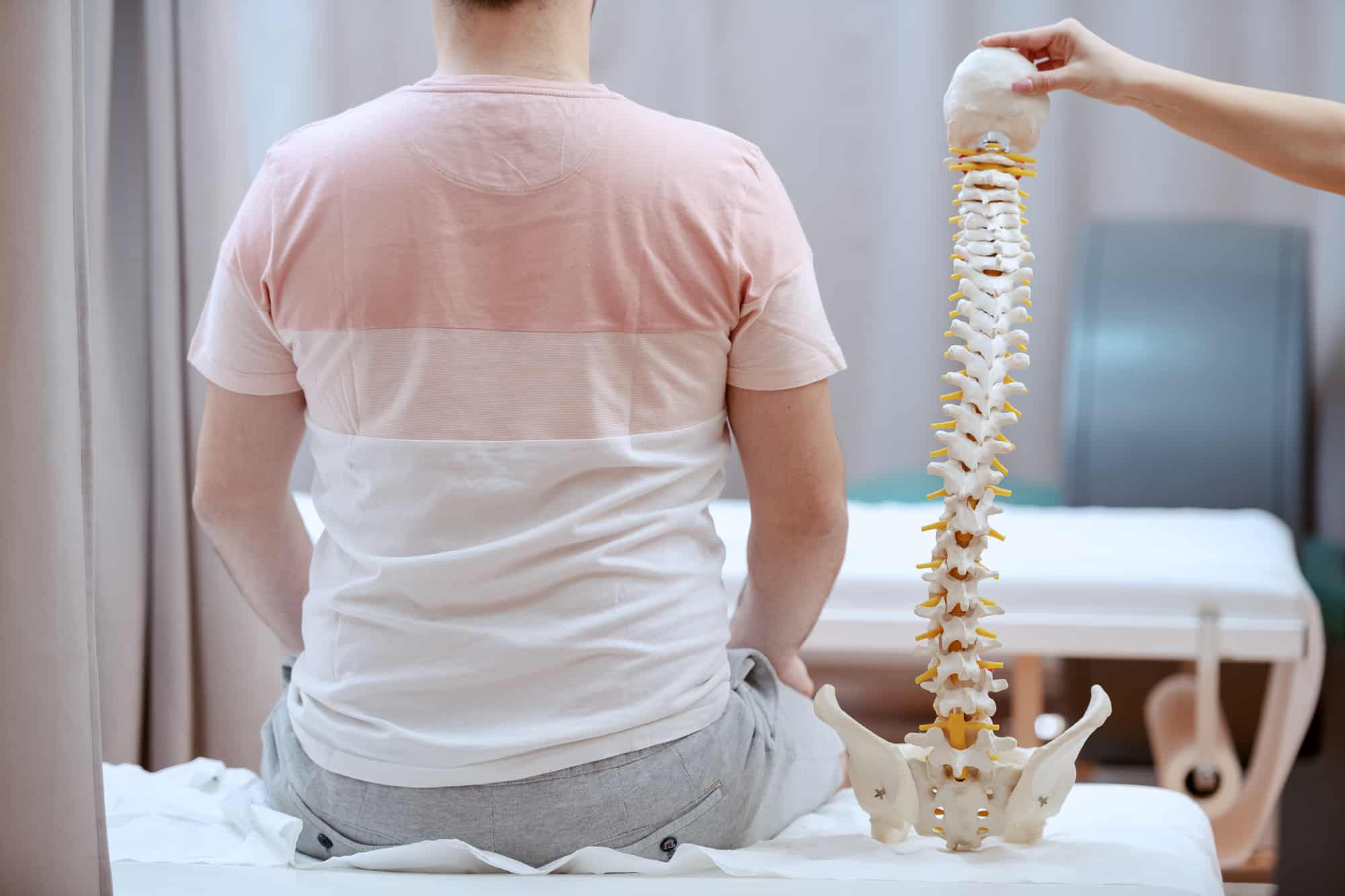 A female doctor is holding a spine model and trying to identify the source of the patient's pain.