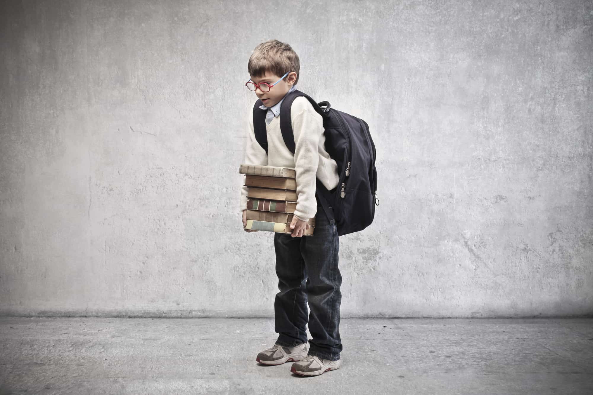 A young boy is carrying a big school backpack