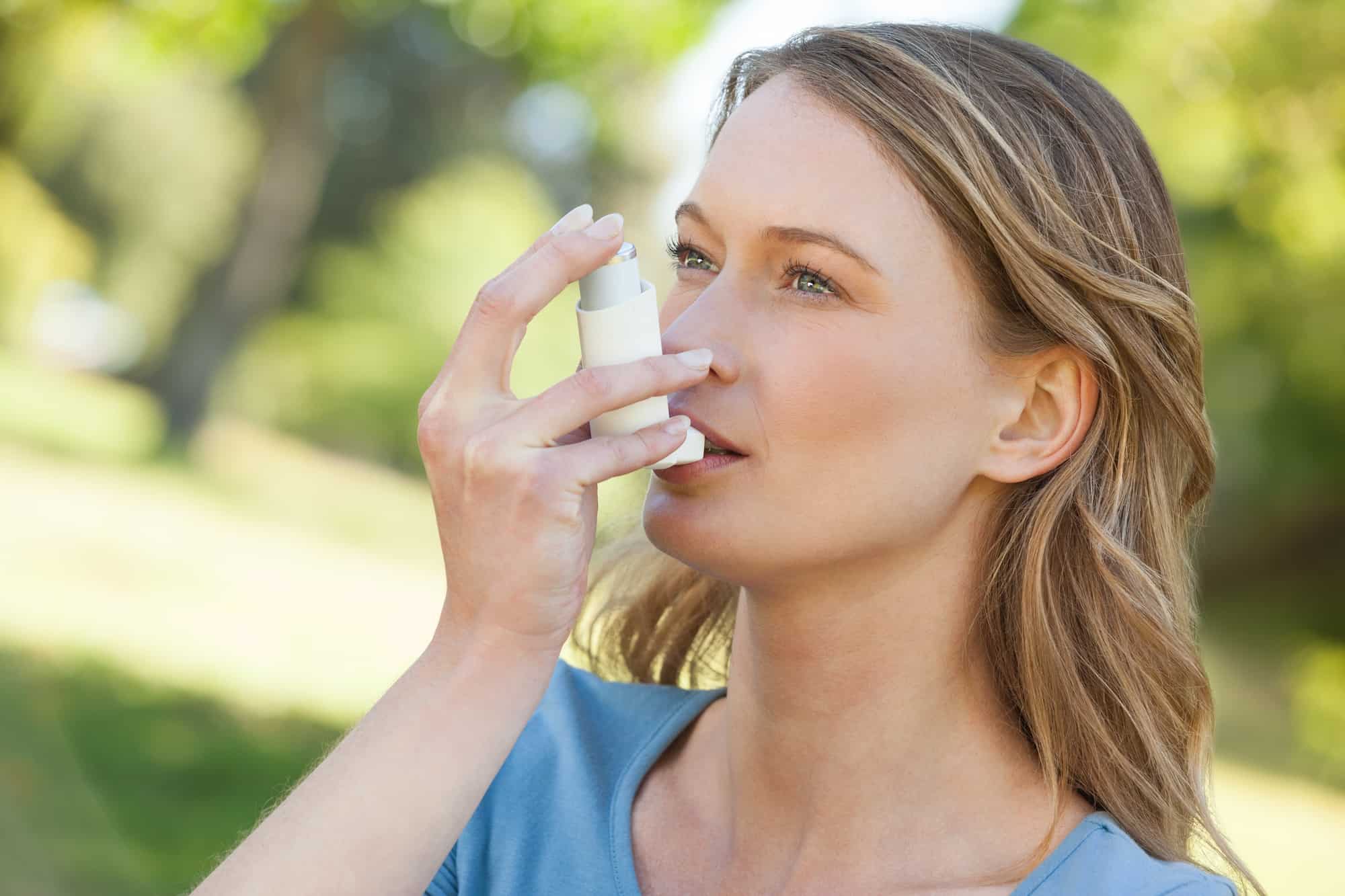 A young woman using asthma inhaler in the park