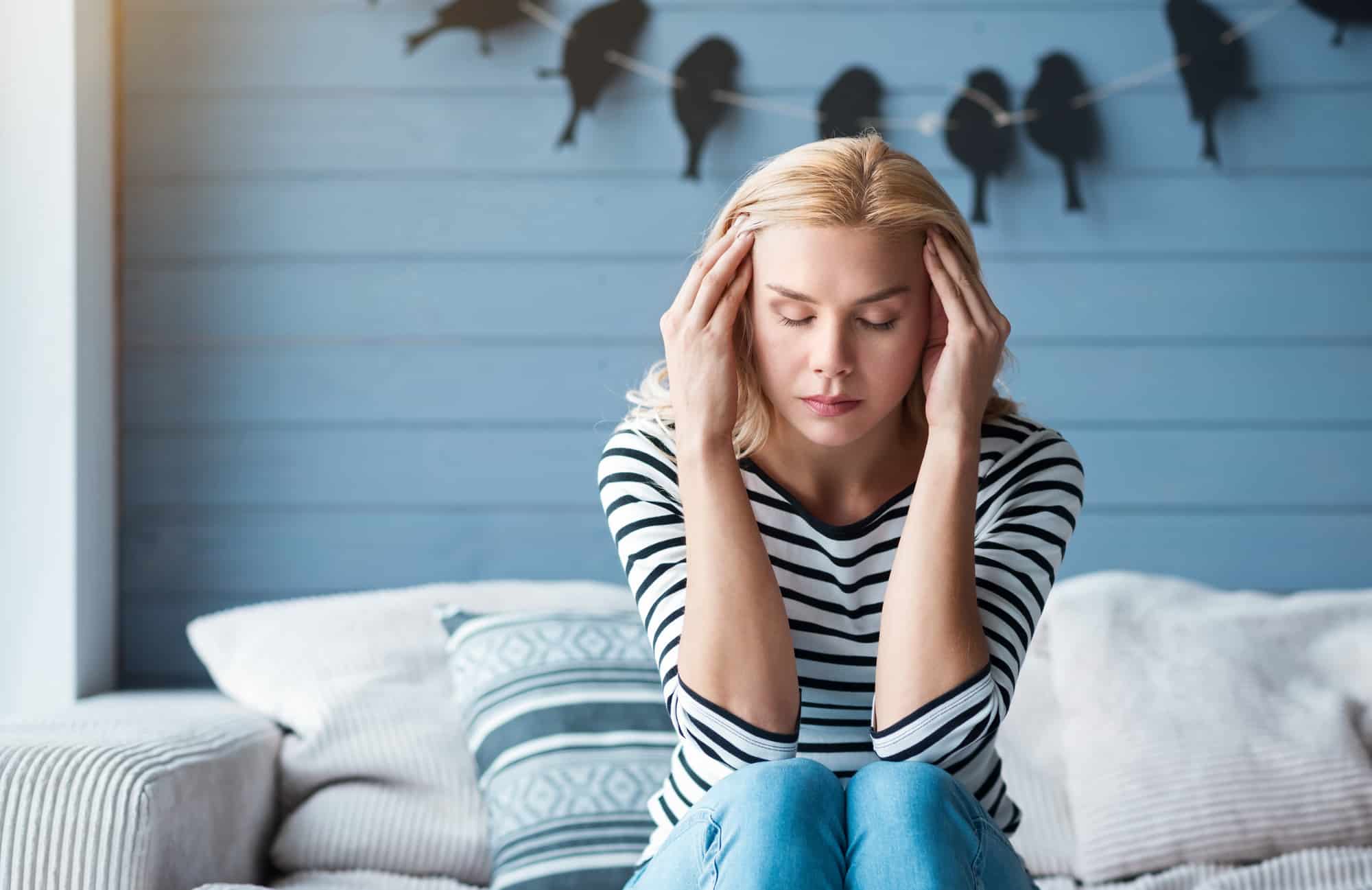 A woman is sitting on a couch with a bad headache