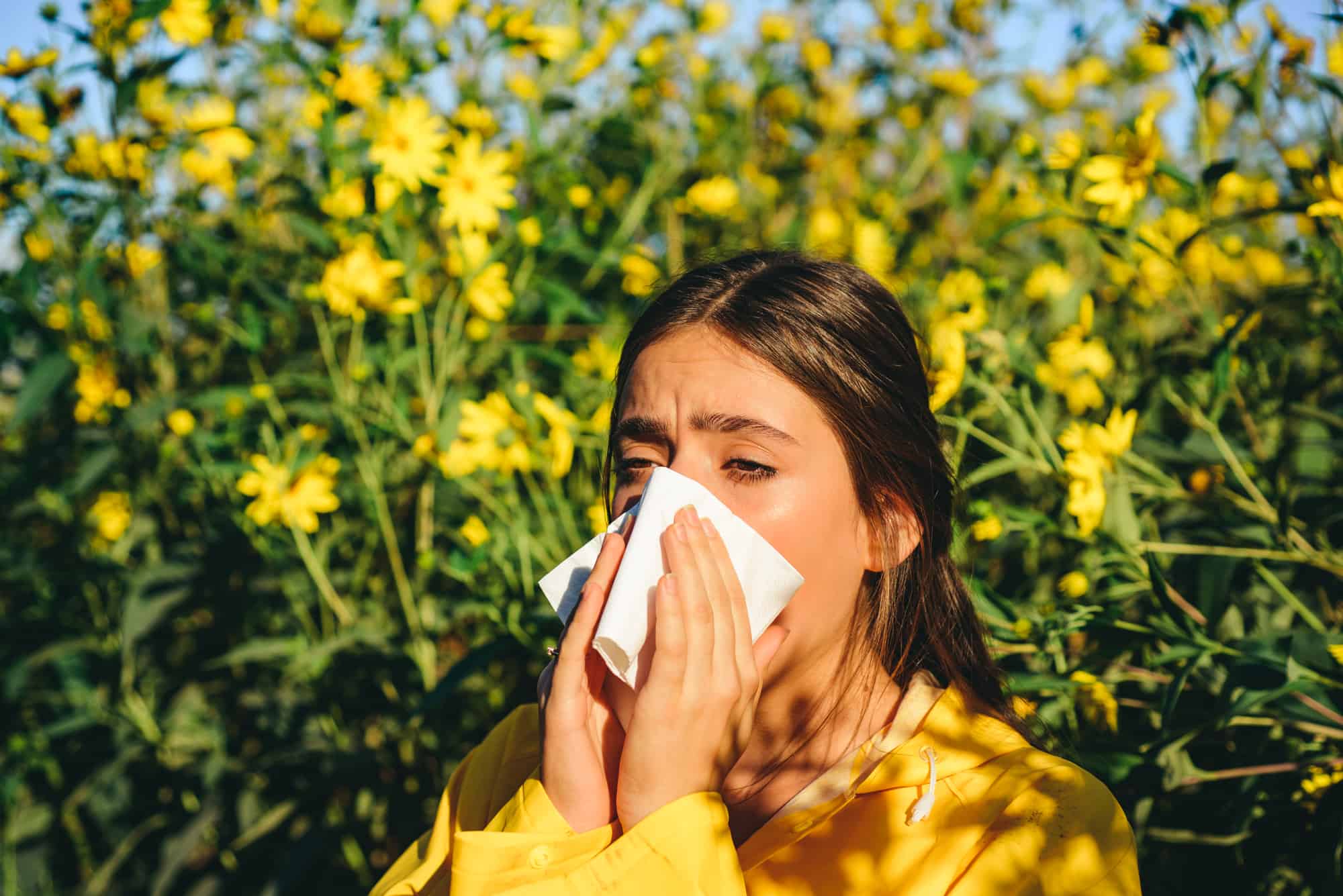 A woman is sneezing and has a runny nose due to pollen allergy