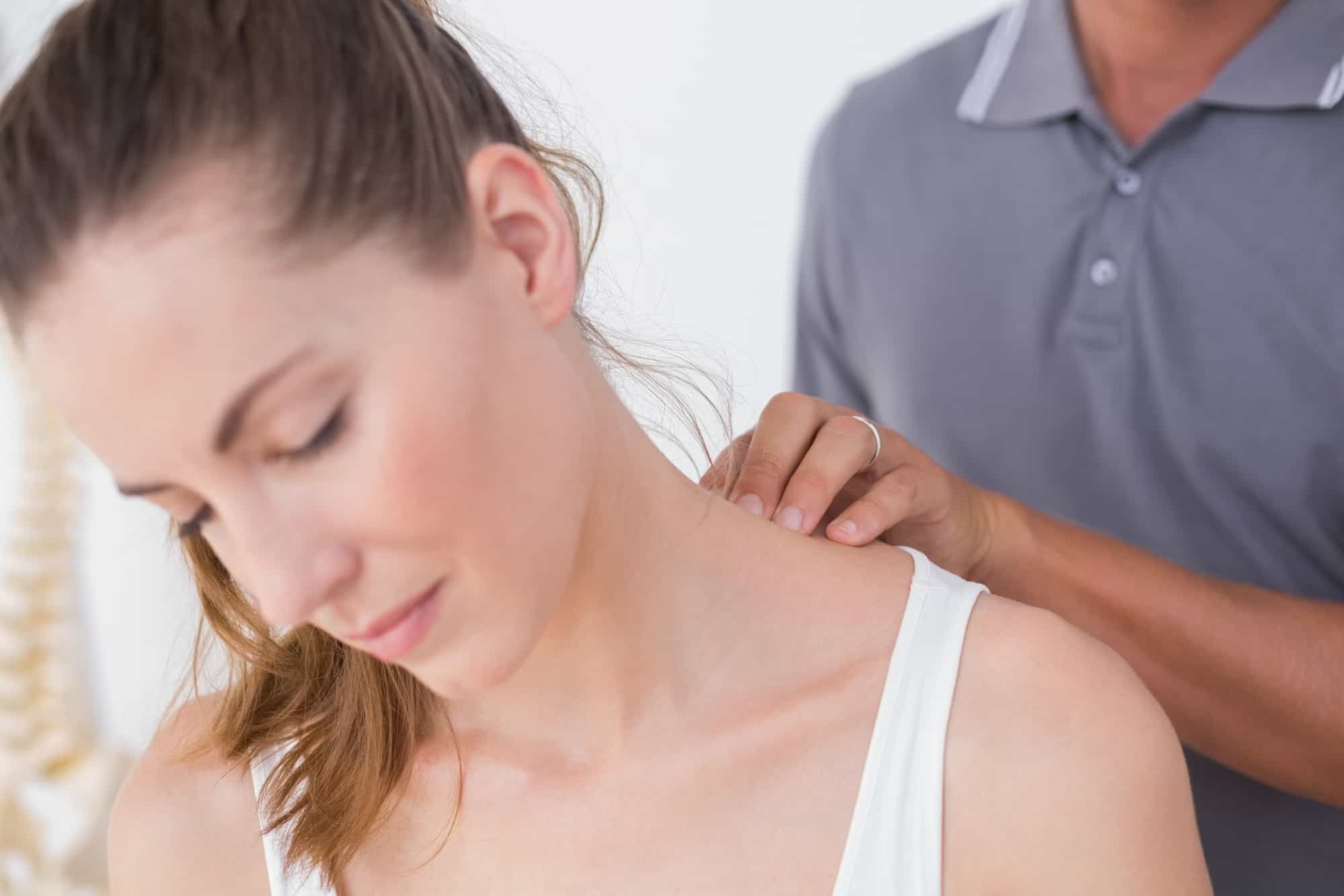 A chiropractor is performing a neck adjustment on a woman to address her frozen shoulder due to stress