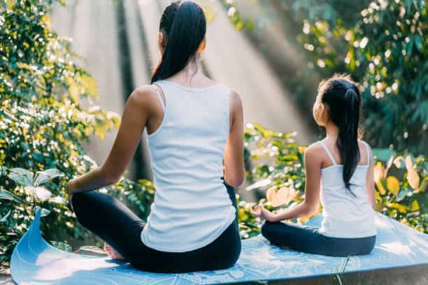 Mother and daughter meditating in rainforest