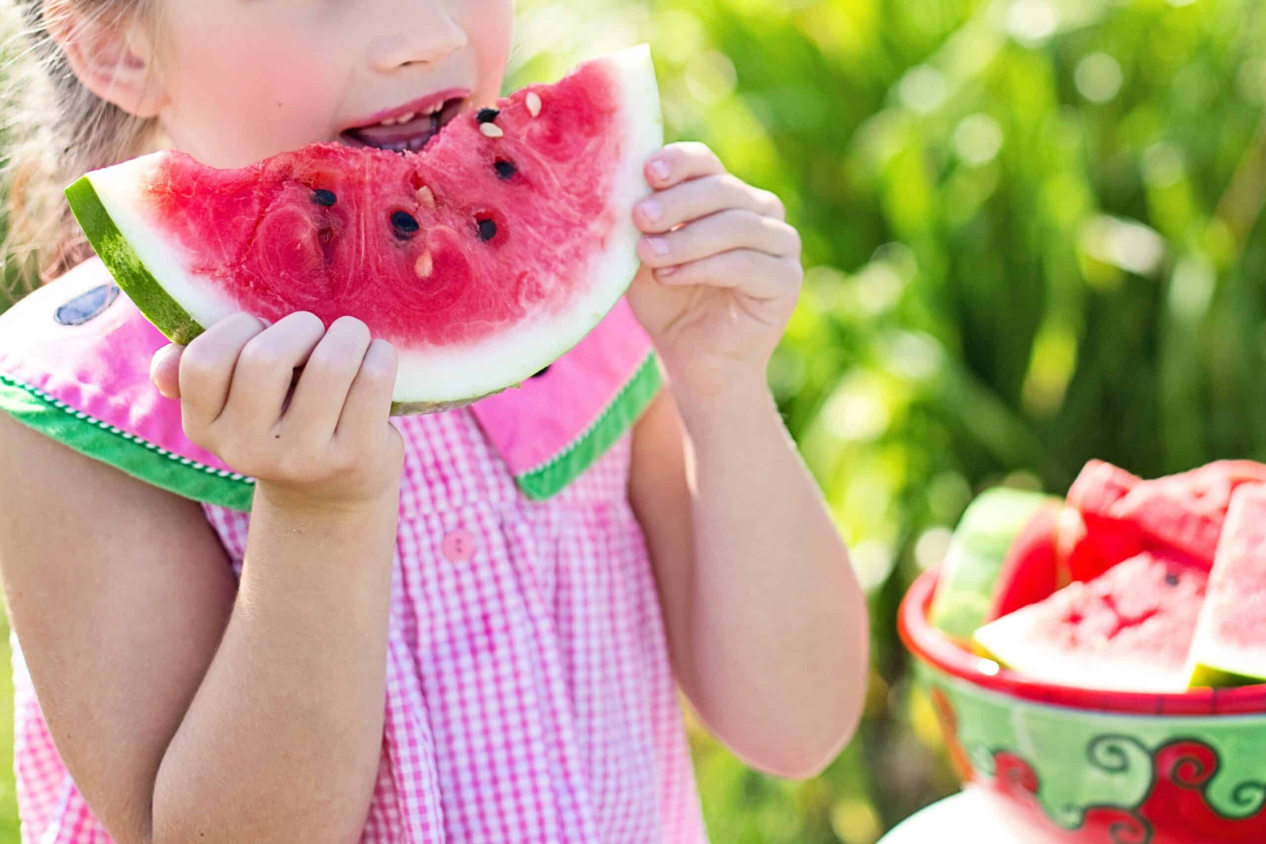 a little girl eating a slice of watermelon